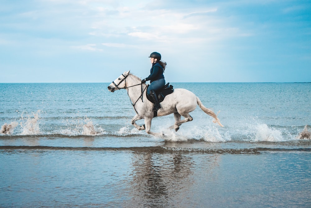 man in black jacket riding white horse on water during daytime