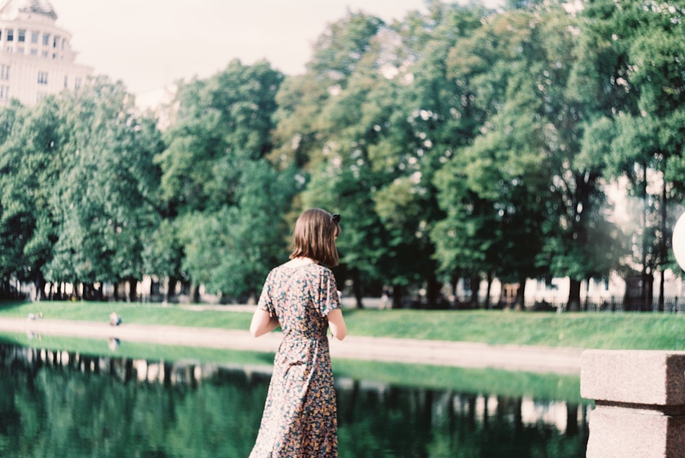 woman in black and white floral dress standing near green grass field and body of water