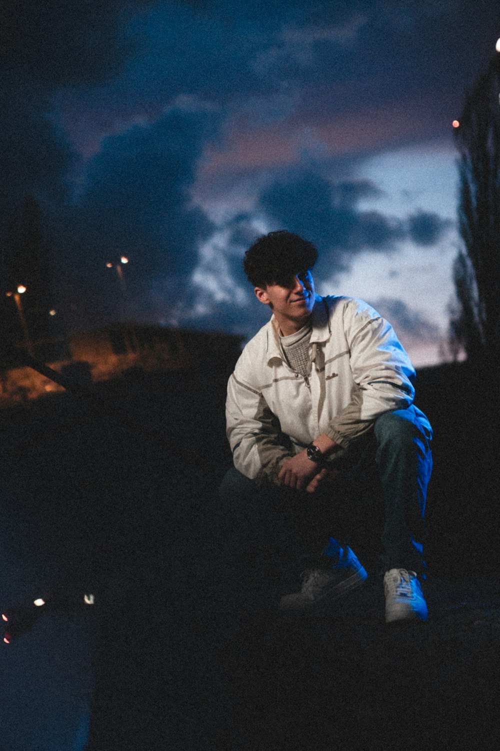 homem em jaqueta branca e jeans azuis sentados na rocha durante a noite