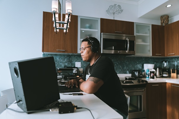 A professional chef working on a laptop in a modern kitchen with dark tones and green accents.
