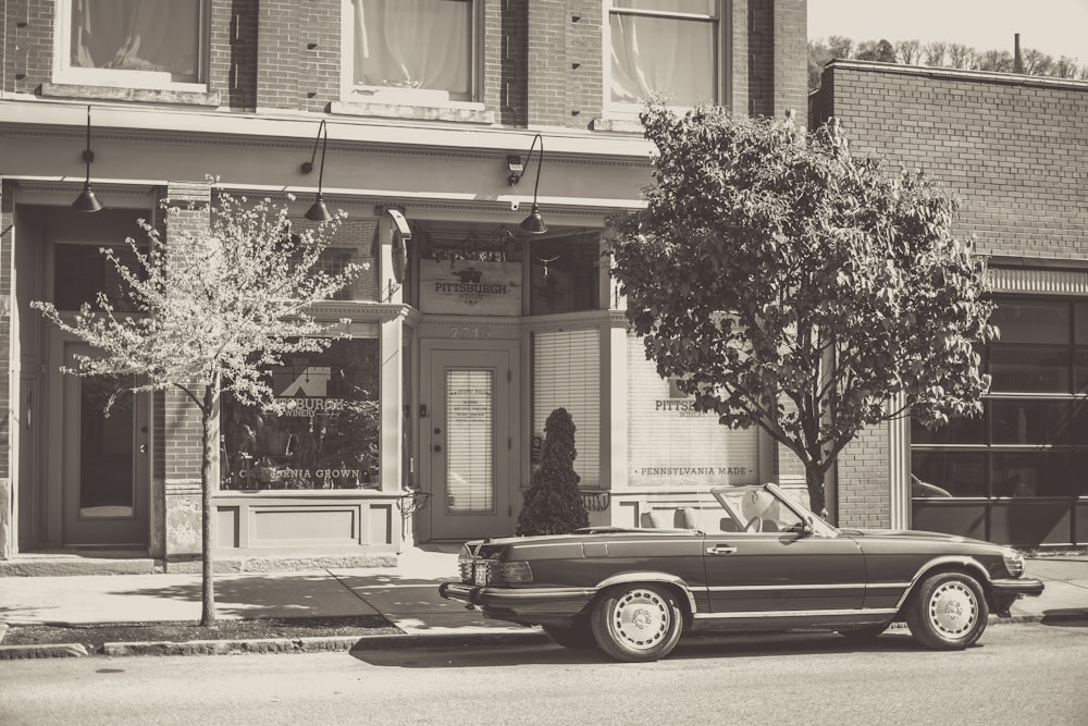 grayscale photo of car parked beside building