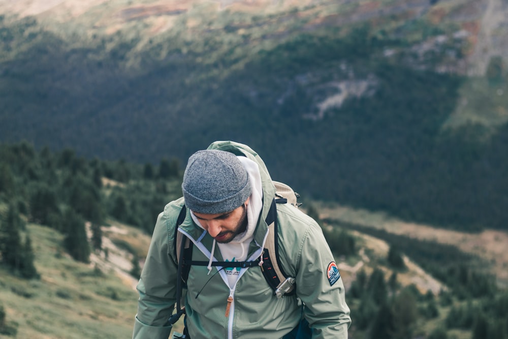 man in green jacket and gray knit cap standing on brown rock mountain during daytime