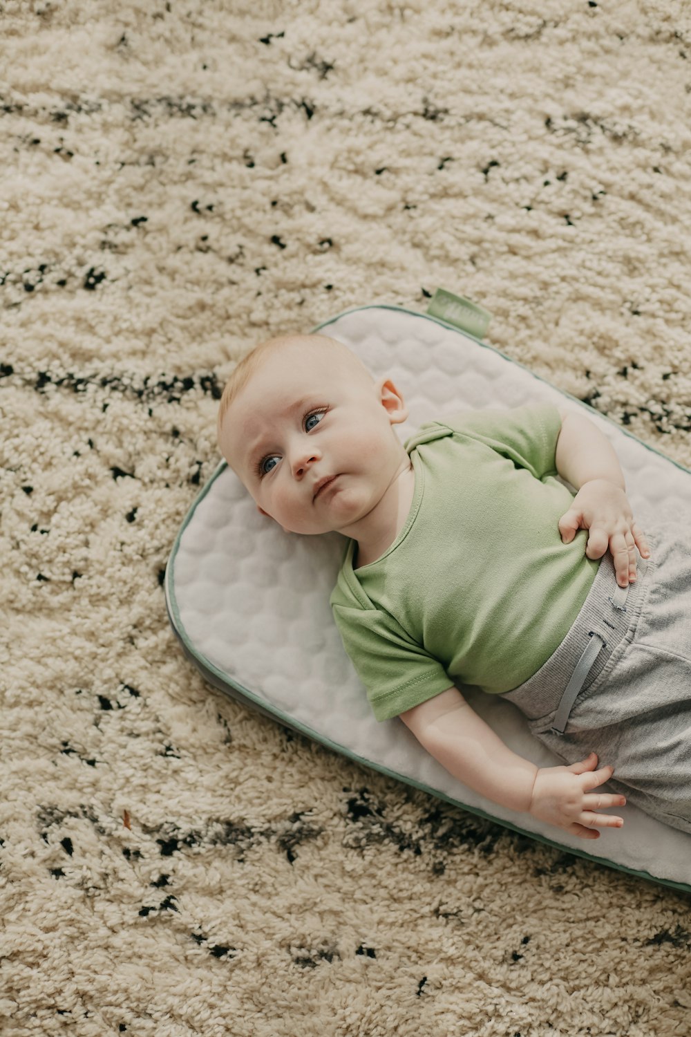 Baby in grünem Onesie liegt auf weiß-blauem Polka-Dot-Bett