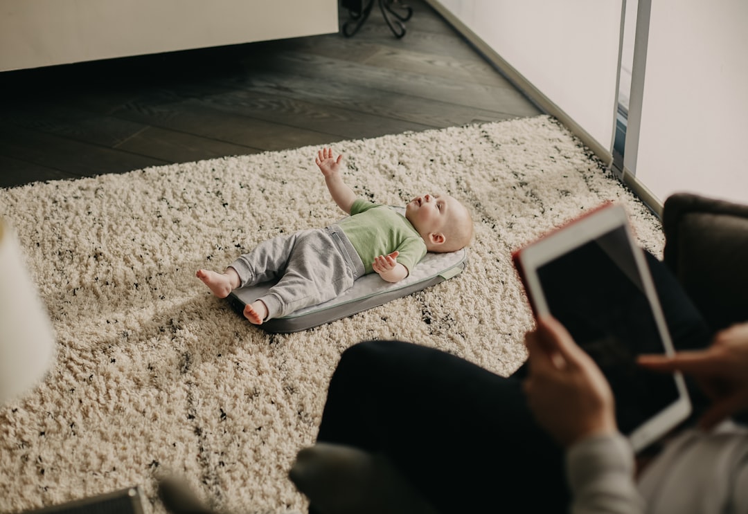 baby lying on floor beside person in black pants