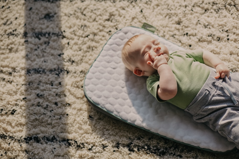 baby in green onesie lying on white and gray textile