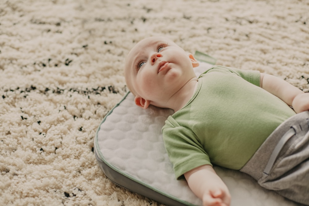 baby in green onesie lying on white and gray bed