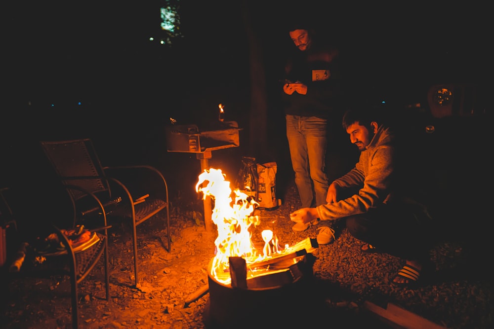 man in black jacket sitting beside fire pit during nighttime