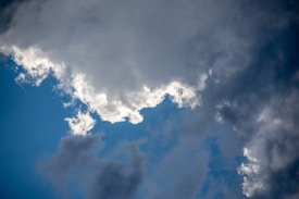 Large cloud formations fill the sky, with patches of bright blue visible in between. The clouds are a mix of white and darker gray tones, indicating a dynamic and possibly changing weather condition.