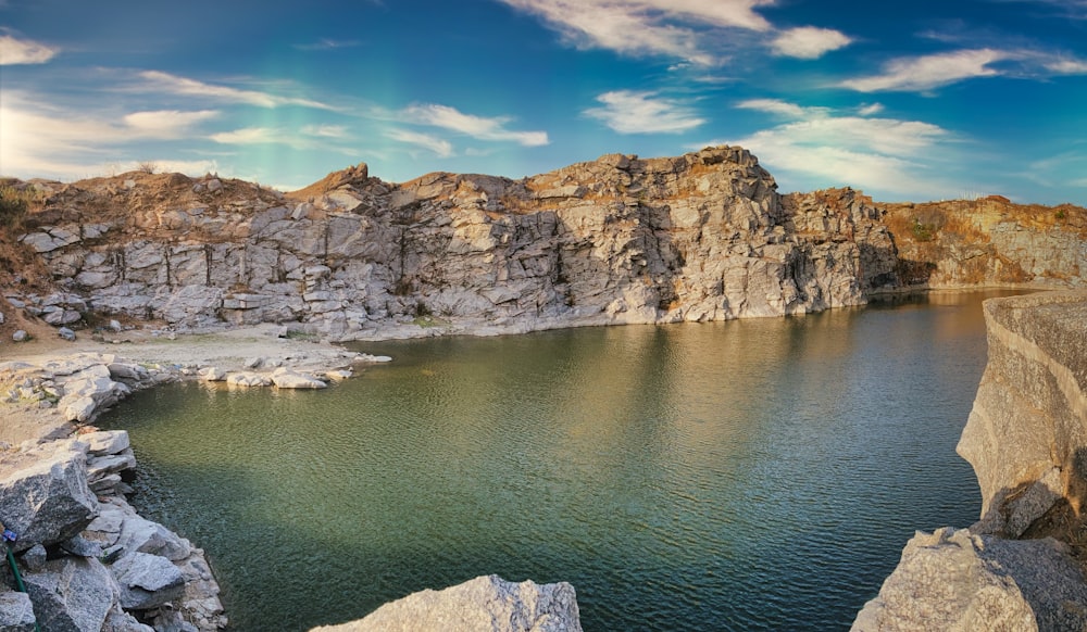 gray rocky mountain beside body of water under blue sky during daytime