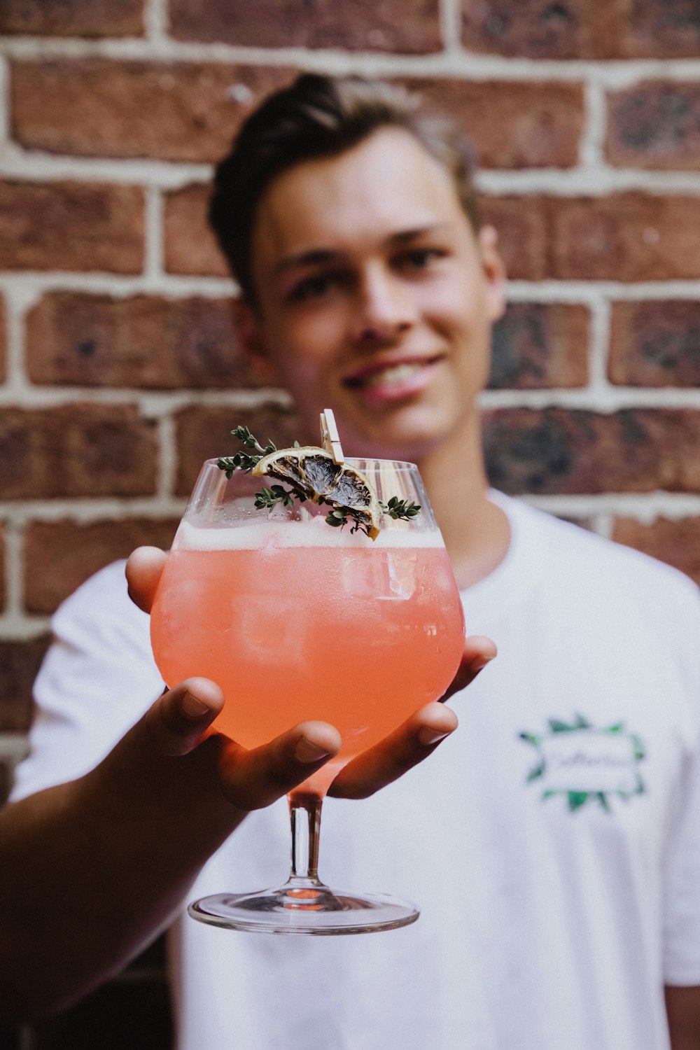 a man holding a drink in front of a brick wall