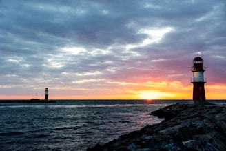 silhouette of lighthouse near body of water during sunset