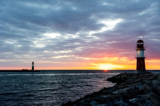 silhouette of lighthouse near body of water during sunset