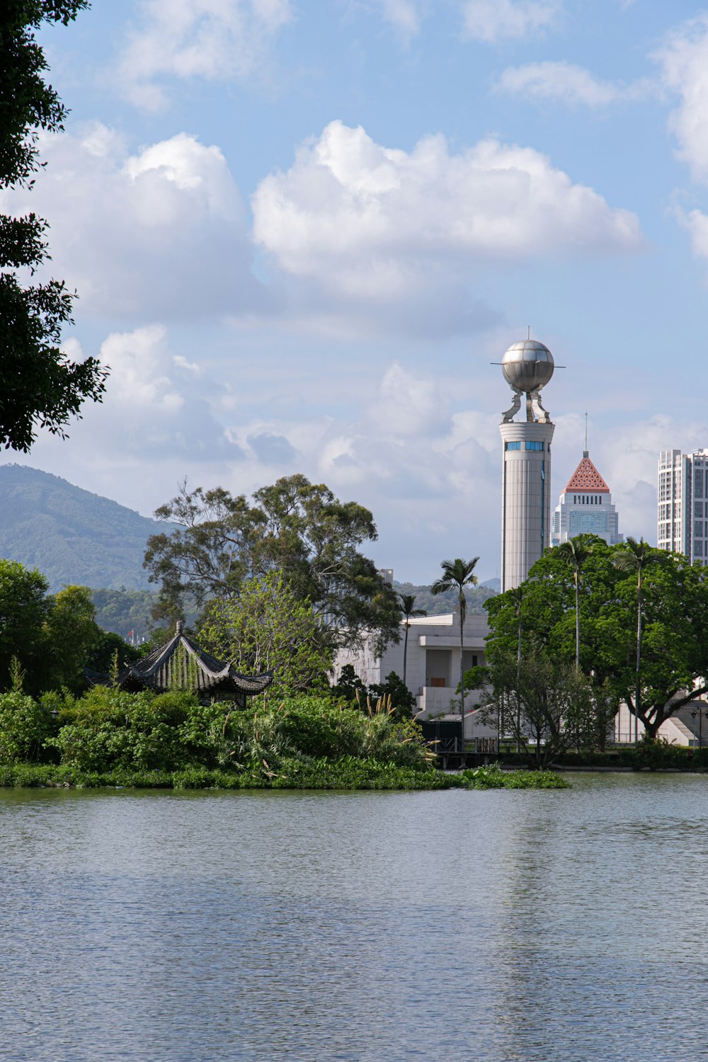 white concrete building near green trees and lake under white clouds during daytime