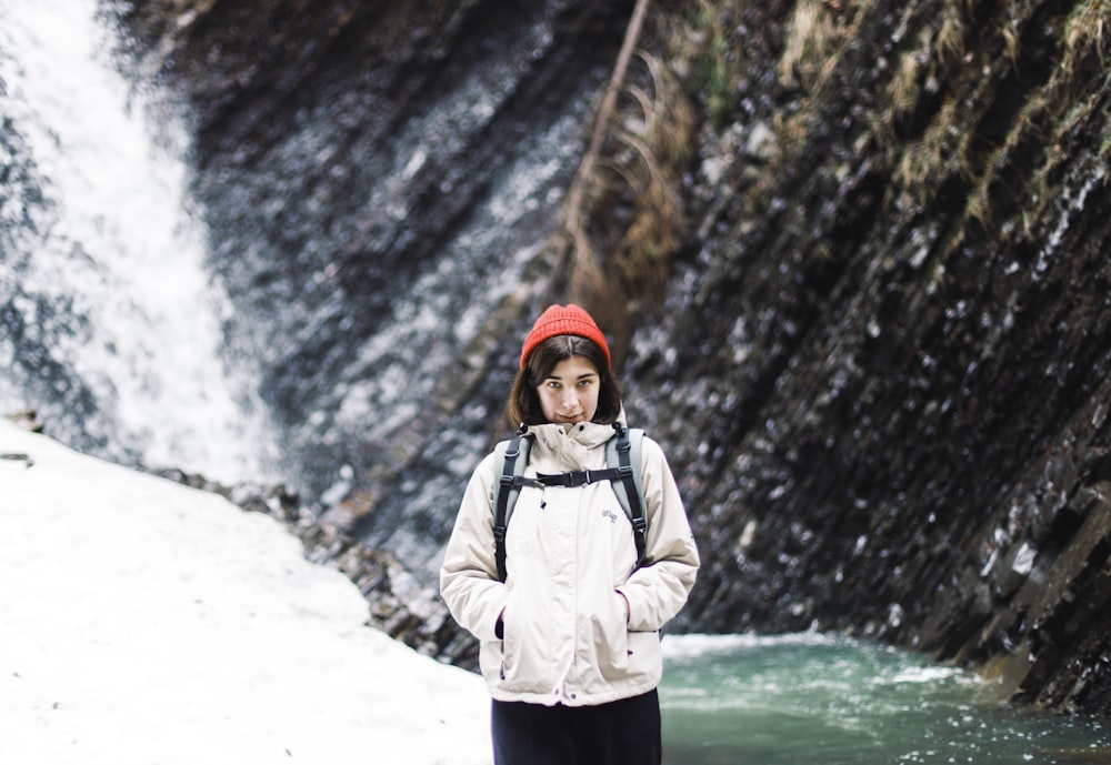 woman in gray jacket standing on snow covered ground near waterfalls during daytime