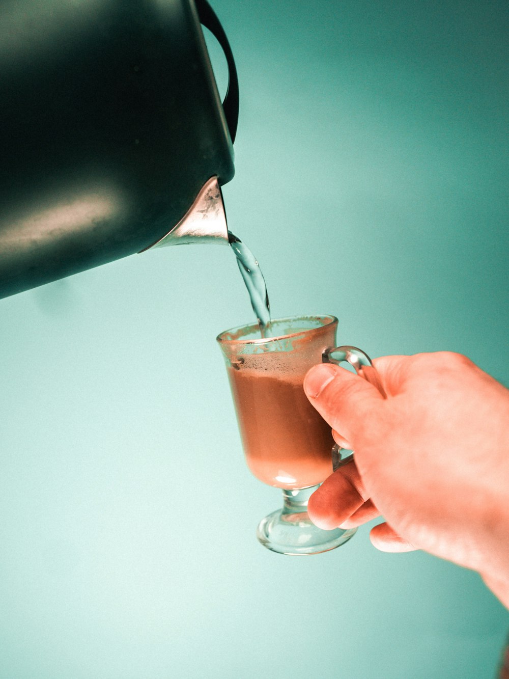 person pouring brown liquid on clear drinking glass