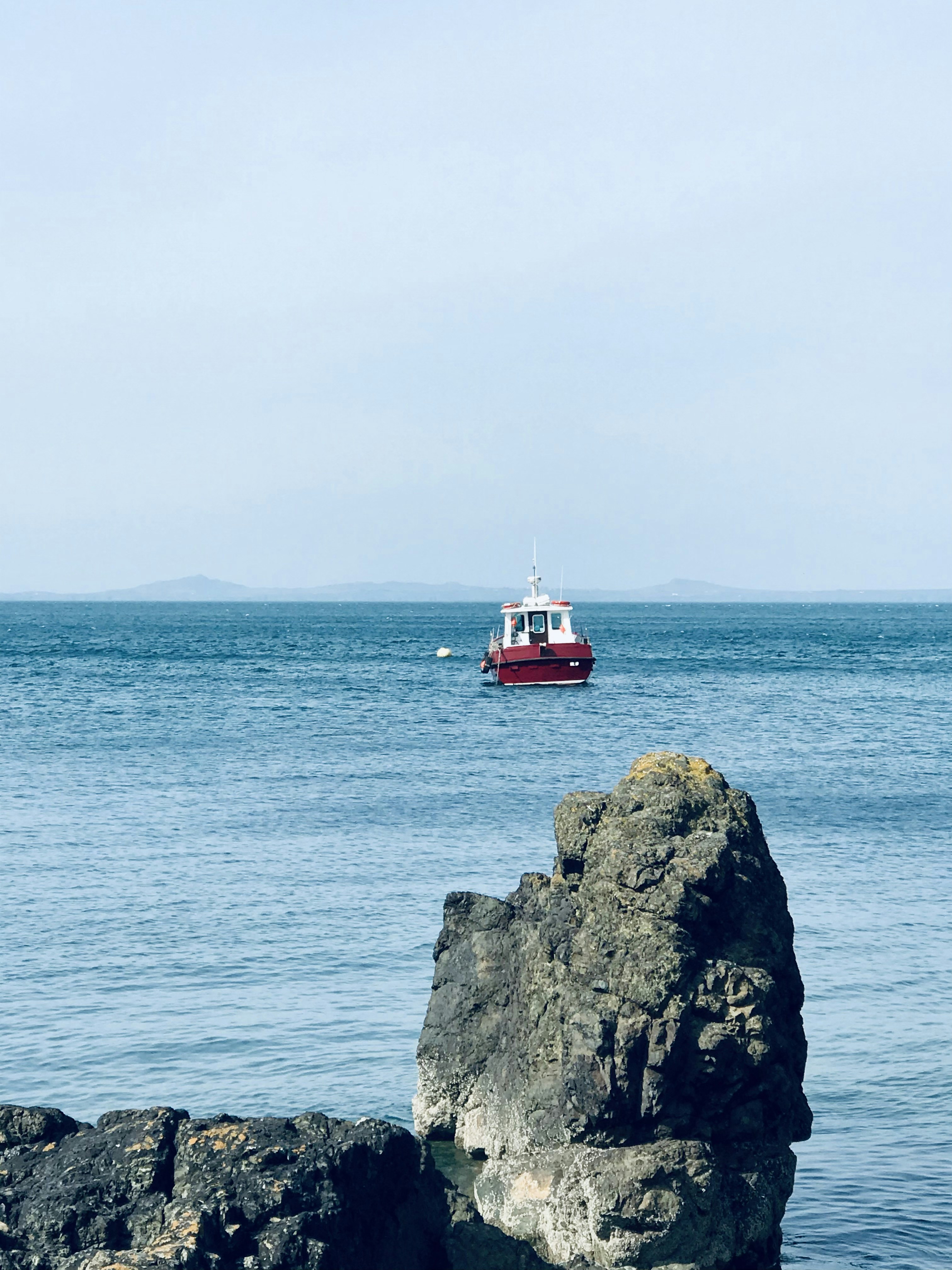 red and white boat on sea near gray rock formation during daytime