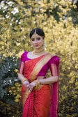 A graceful woman draped in a vibrant Benares saree standing against a golden-hued background.