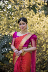 A graceful Indian woman draped in a luxurious silk saree, standing against a soft cream backdrop with subtle gold accents.