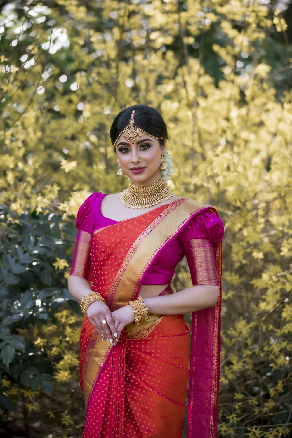 woman in red and white sari standing near green trees during daytime