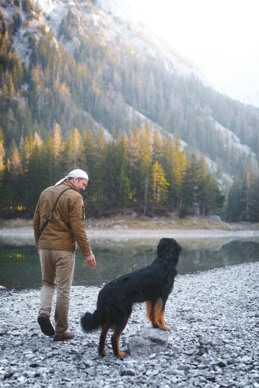 man in brown jacket and brown pants standing beside black dog on snow covered ground during