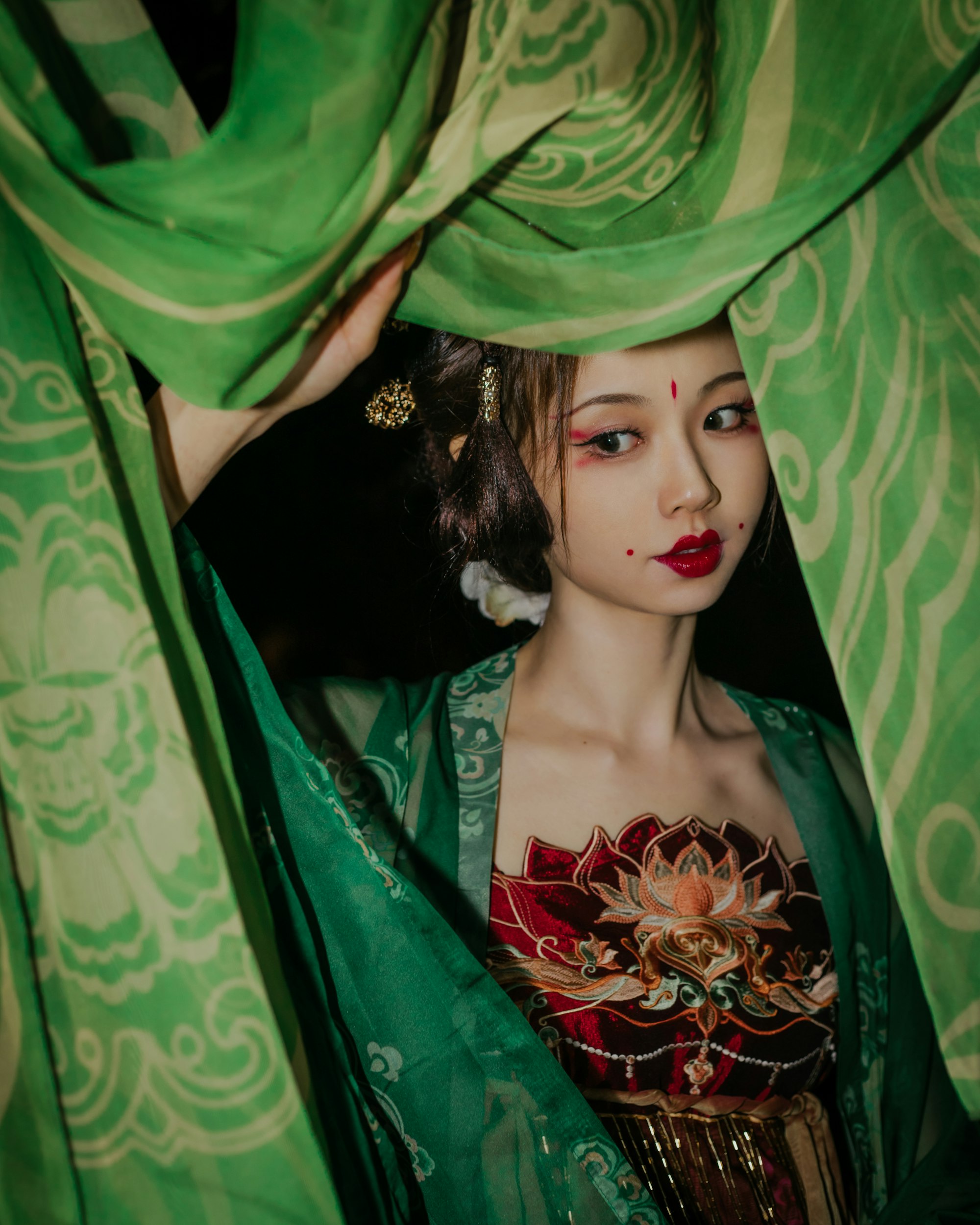 Woman peeking out of green sheets covering a doorway