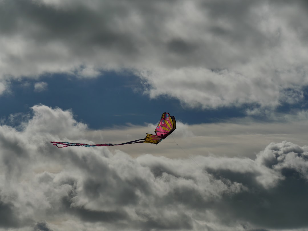 yellow and red kite flying under white clouds during daytime