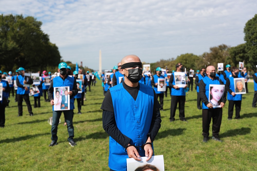 homme en chemise à manches longues bleue portant des lunettes de soleil noires debout sur un champ d’herbe verte pendant la journée