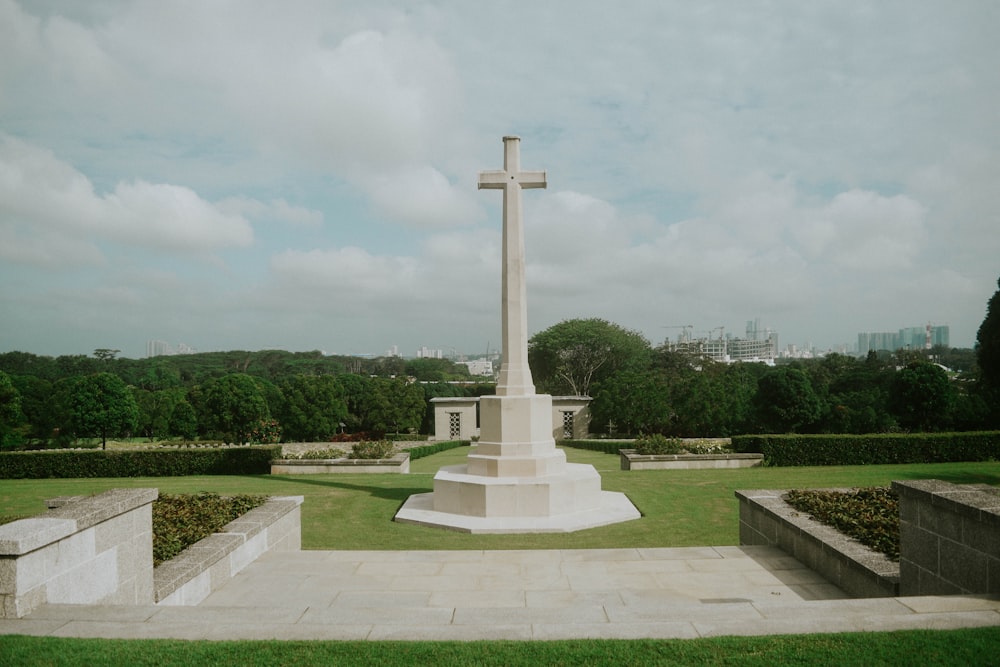 white concrete cross statue on green grass field under white clouds during daytime