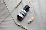 Close-up of Nouréa Elixir bottle with hibiscus flowers and argan nuts on a cream beige background.