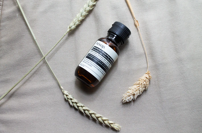 Close-up of a handcrafted amber glass bottle filled with nourishing hair oil surrounded by fresh botanicals.