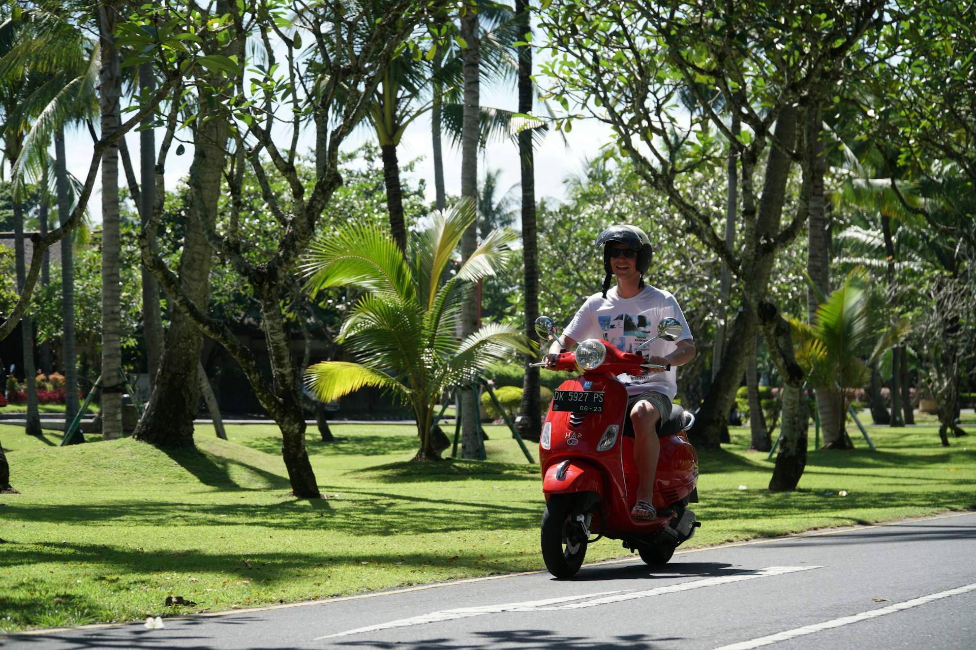 man in white shirt riding red motor scooter on road during daytime