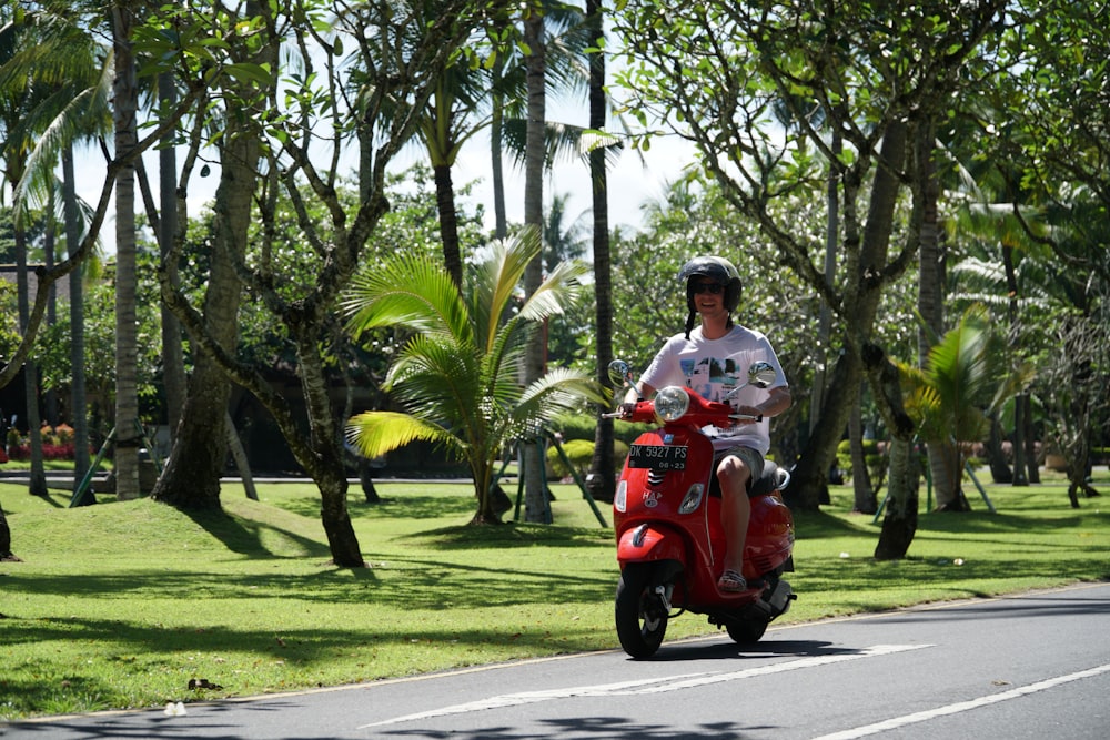 man in white shirt riding red motor scooter on road during daytime