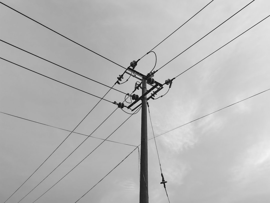 grayscale photo of electric post under cloudy sky