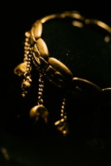 A close-up of an ornate gold bracelet with several dangling chain elements. The bracelets have a lustrous shine against a dark background, which highlights its intricate design.
