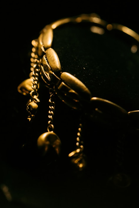 Close-up of a delicate gold bracelet with intricate detailing resting on a velvet cushion.