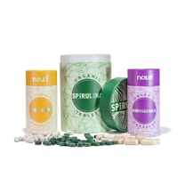 Collection of three cylindrical containers with labels for different dietary supplements. The containers are designed with various colors: yellow for Lion's Mane, green for Spirulina, and purple for Ashwagandha. White and green capsules are scattered around the containers.