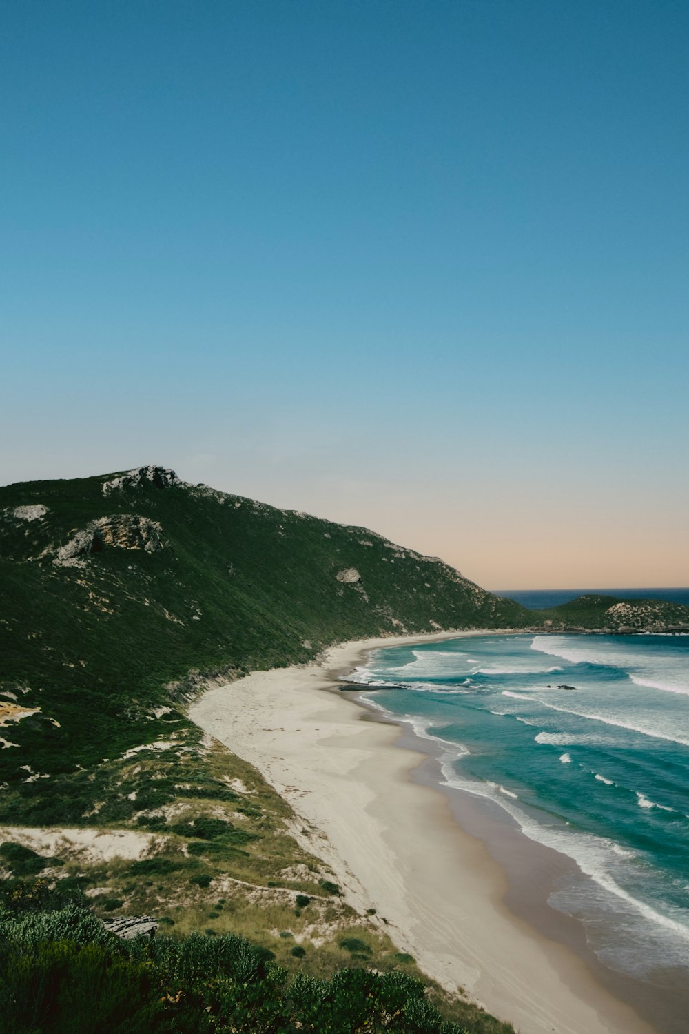 green mountain beside blue sea under blue sky during daytime