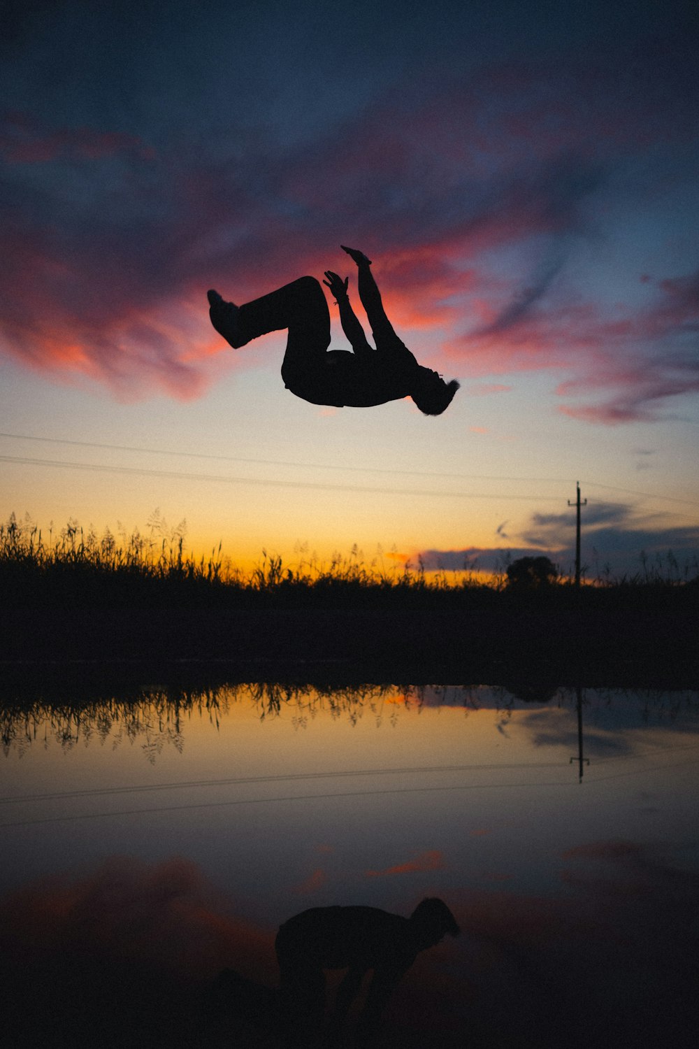 Silhouette einer Person, die während des Sonnenuntergangs auf dem Wasser springt