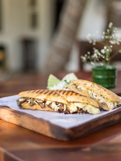 Close-up of a golden, toasted panini filled with melted cheese and fresh greens on rustic wooden board.