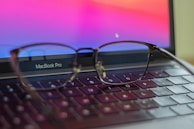 A stylish pair of blue-cut lens glasses displayed beside a laptop, emphasizing eye protection for screen time.