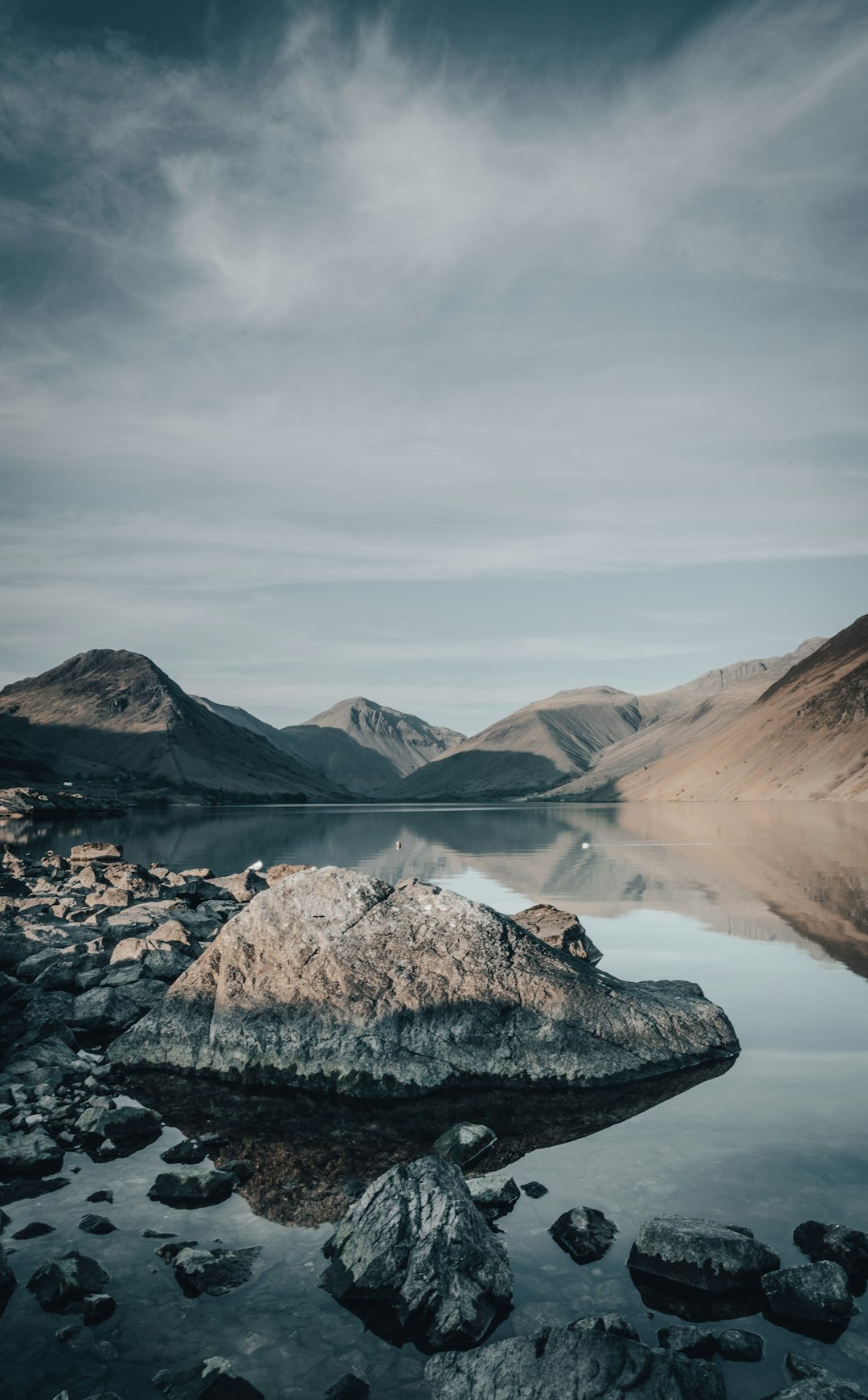 rocky mountain near lake under cloudy sky during daytime