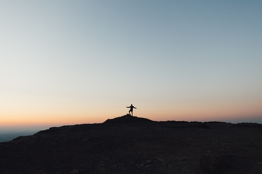 silhouette de personne debout sur la formation rocheuse pendant le coucher du soleil