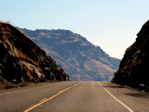 Aerial view of a newly paved highway cutting through mountainous terrain under clear skies.
