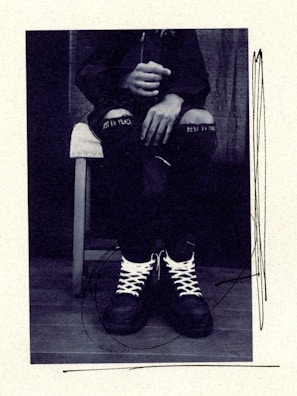 man in black jacket and black and white striped pants sitting on white chair