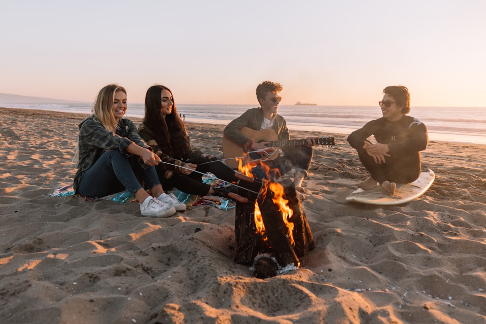 man and woman sitting on sand near bonfire during daytime