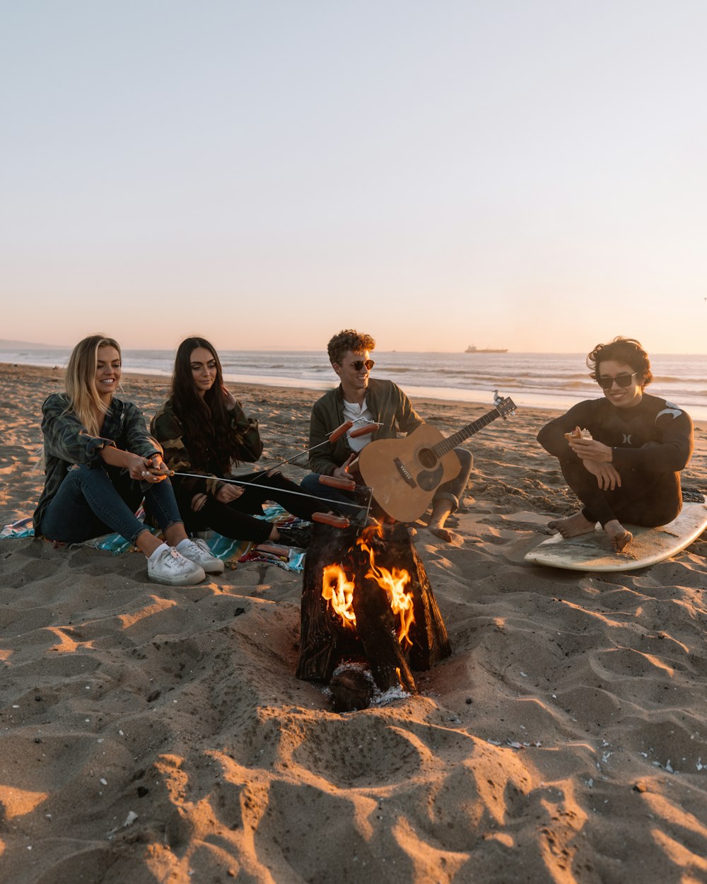 people sitting on sand near bonfire during daytime