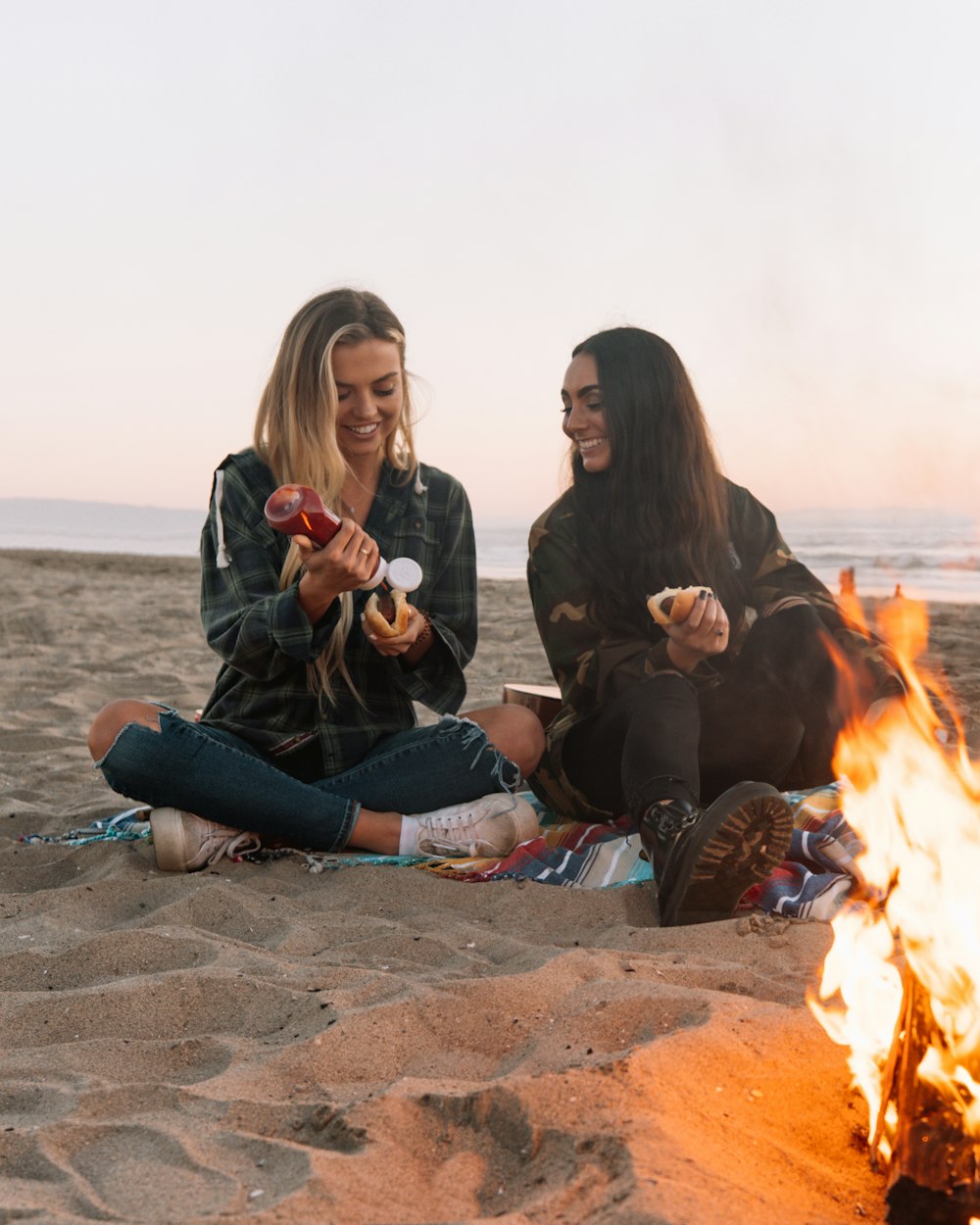 3 women sitting on brown sand near bonfire during daytime