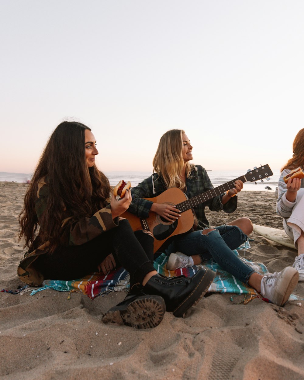 3 donne sedute sulla sabbia marrone che suonano le chitarre durante il giorno