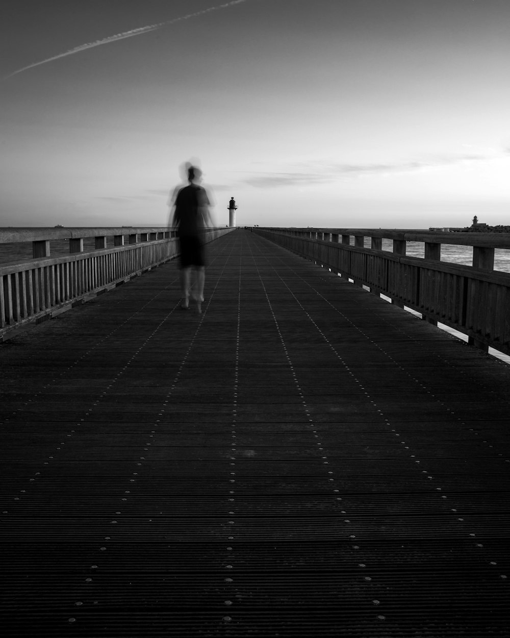 grayscale photo of person walking on wooden bridge