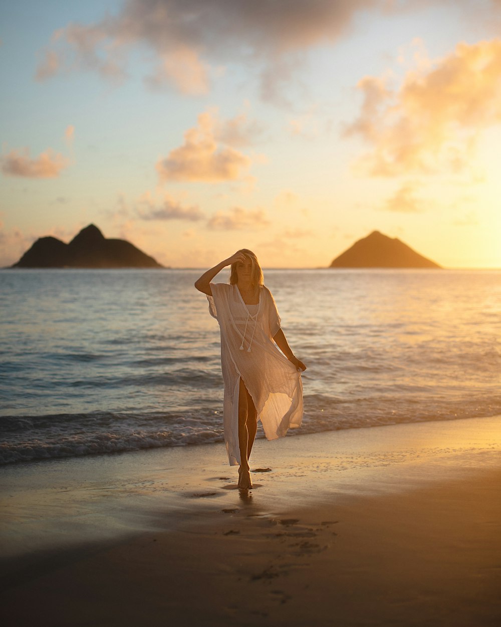 Frau in weißem Kleid steht bei Sonnenuntergang am Strand